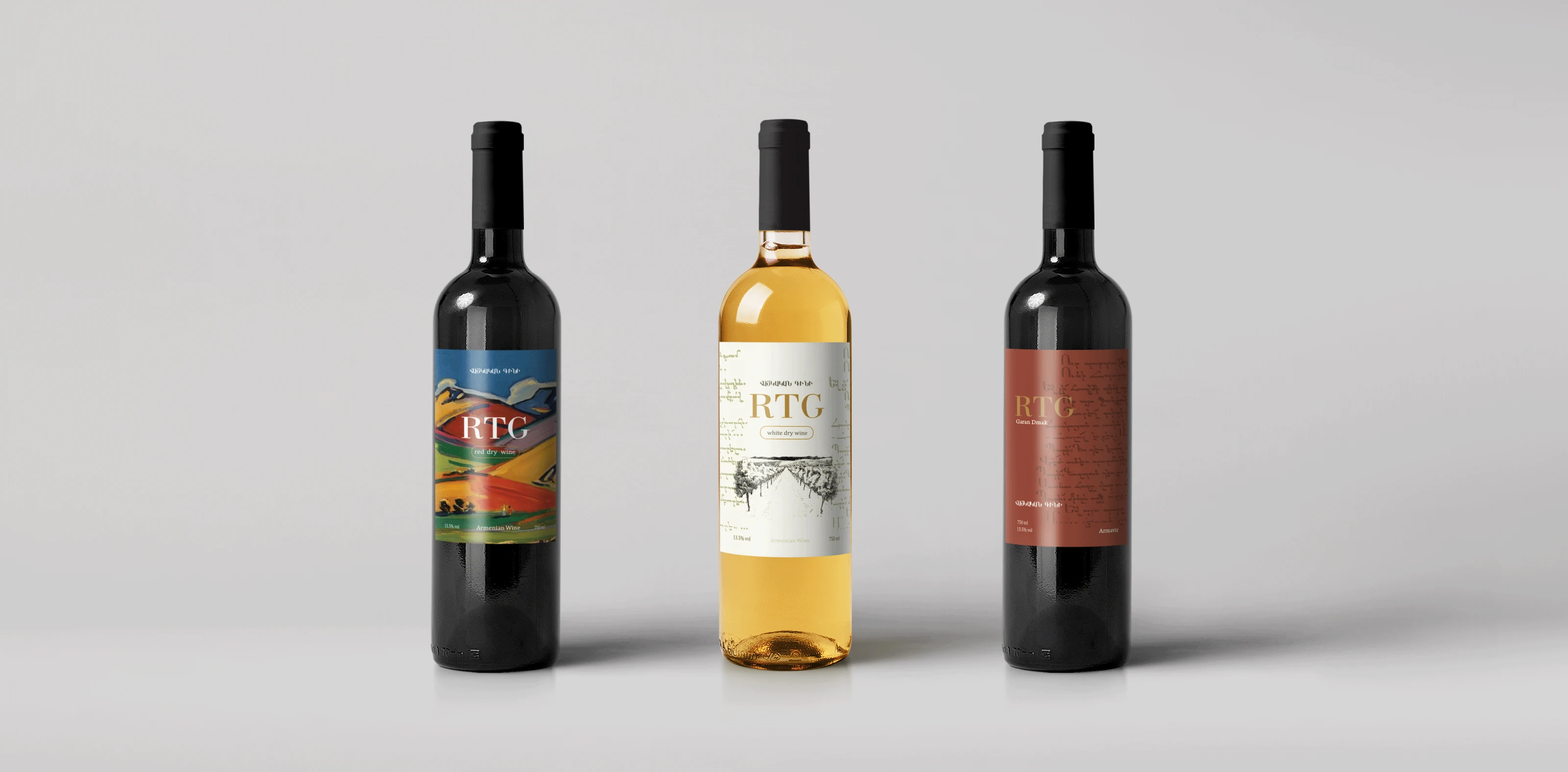 Three wine bottles carrying the RTG mark: a red with a painted landscape label, a white with an engraved vineyard label, and a plain terracotta one.