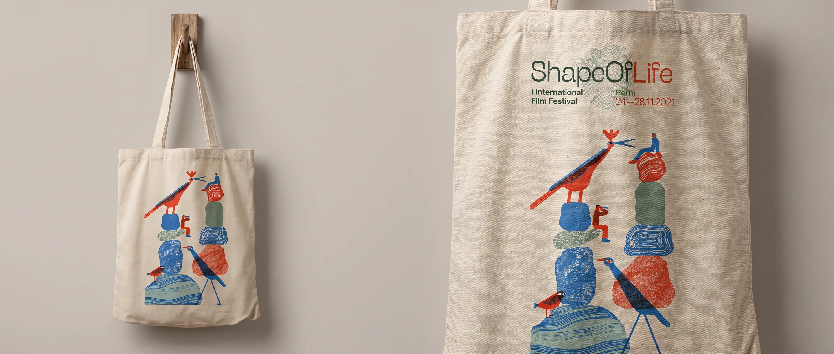 A canvas tote bag on a wooden peg, printed with stacked stones and birds under the English ShapeOfLife lockup and the festival dates.